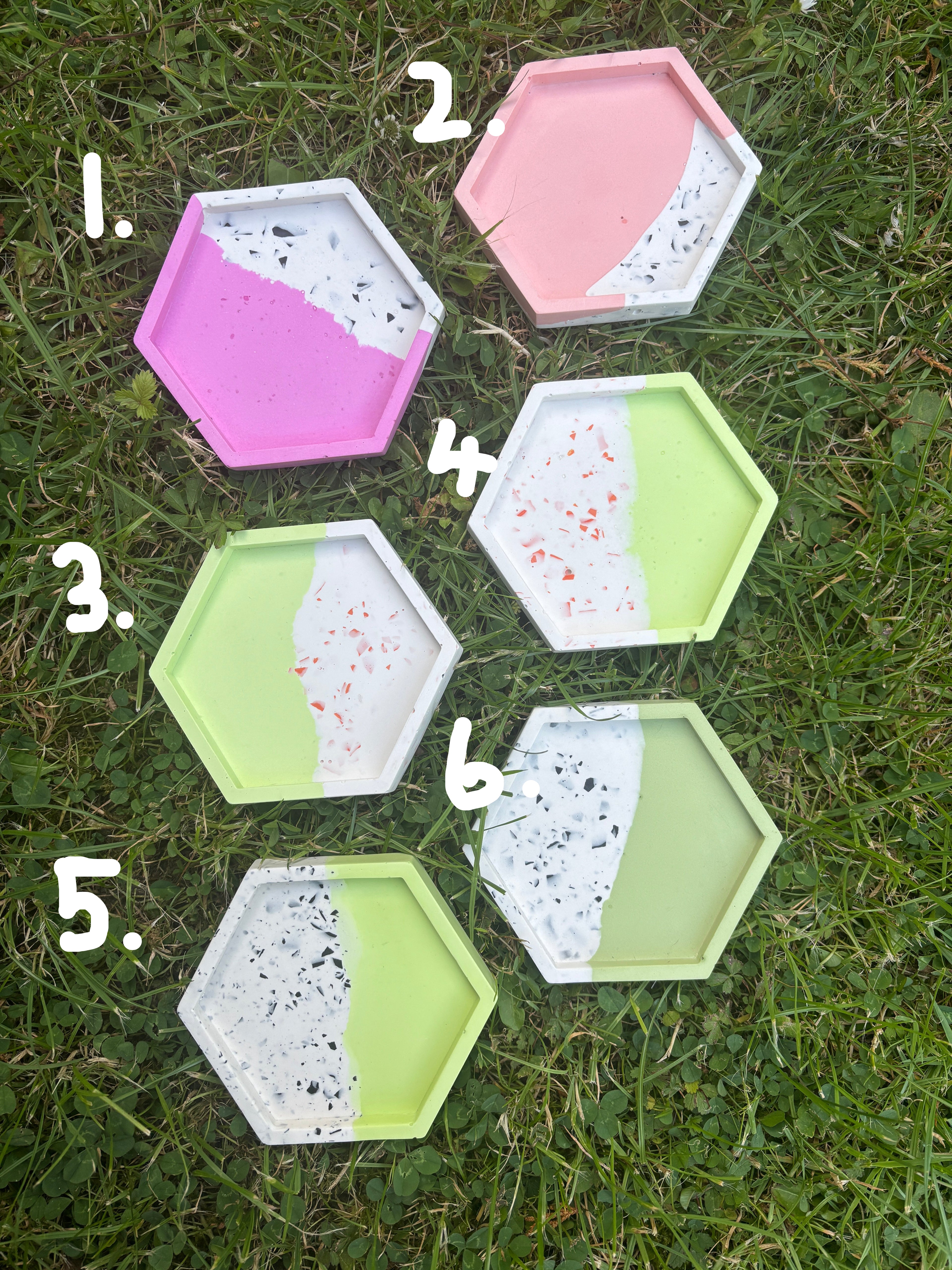 Six hexagonal concrete trays with a terrazzo pattern, painted in pastel pink, purple, green, and white, arranged on a green grass lawn.