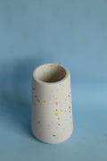 A small cylindrical white ceramic wall-mounted pot with colorful speckles, shown against a light blue background.